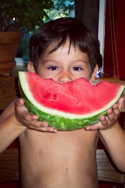 Boy shows a piece of watermelon that he is eating.