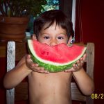 Niño enseña un pedazo de sandia que está comiendo.