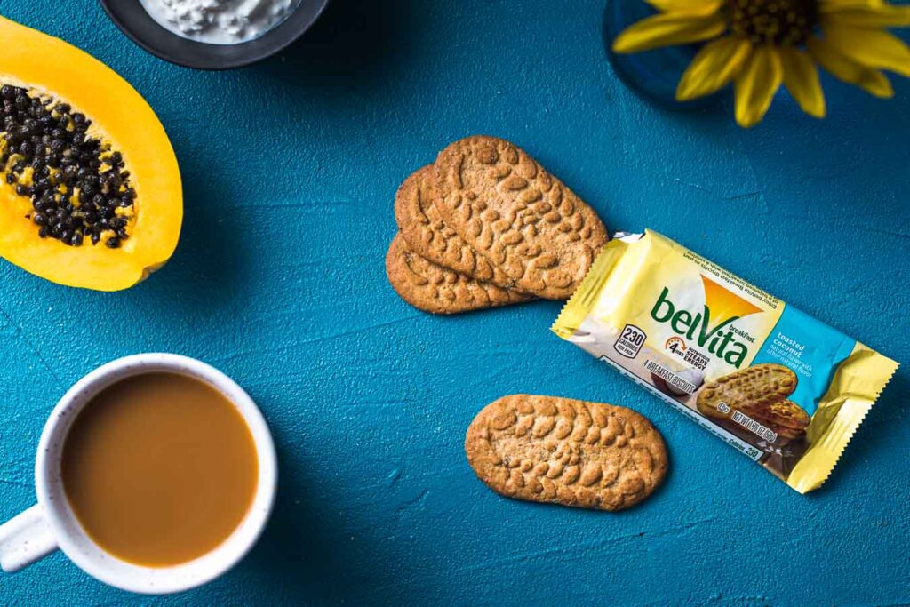 Un paquete de Biscuits belvita abierto, papaya, queso requesón, una taza de café